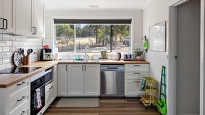 A modern kitchen with white cabinets, a stainless steel dishwasher, and a window overlooking a backyard. - Nanda Lake House: 2  BR, 1  BA Cottage in Bonnie Doon, Sleeps 8 (Bonnie Doon)