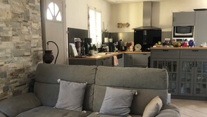 Ein Wohnzimmer mit grauem Sofa, Couchtisch und einer Küchenzeile im Hintergrund.