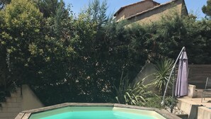 Ein rechteckiger Pool mit Holzdeckrand, umgeben von Bäumen und einem Gebäude im Hintergrund.