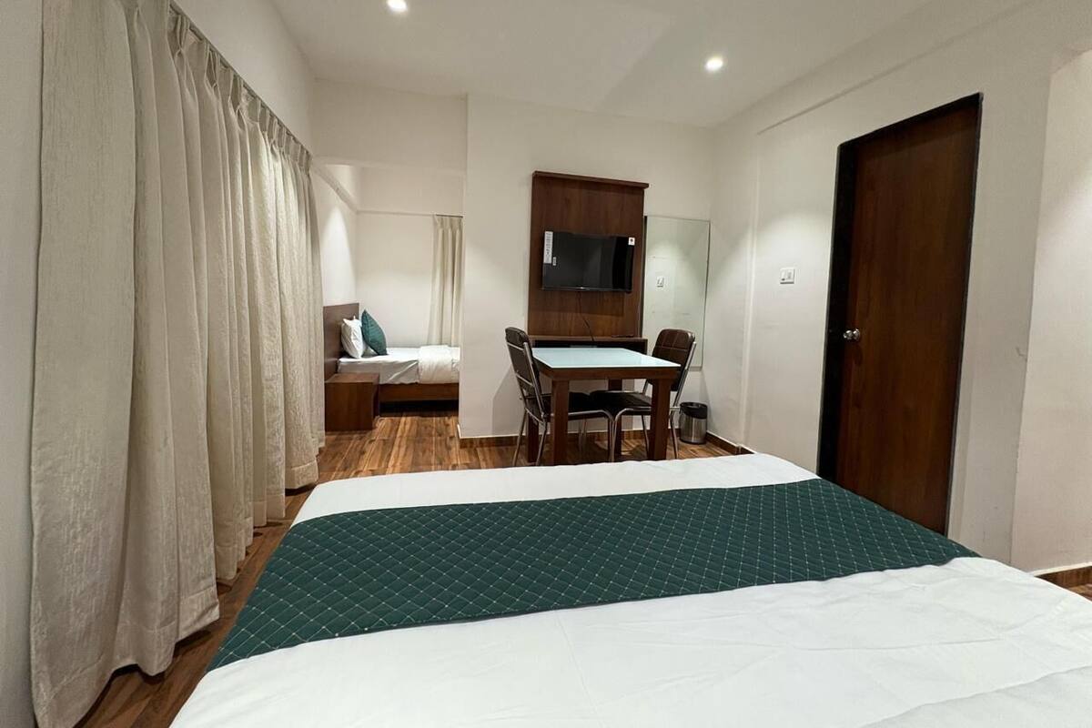 A hotel room with a bed, a desk, a chair, a TV, and a door.