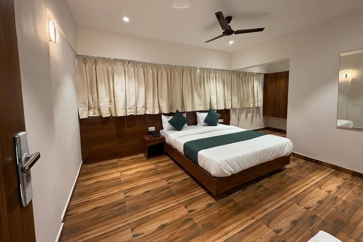 A modern bedroom with a wooden floor, a bed with white bedding and green pillows, a ceiling fan, and a nightstand with a phone.