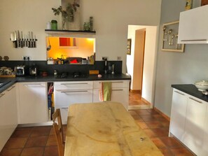 A kitchen with white cabinets, a black countertop, and a wooden table. There are knives hanging on the wall and a sink in the corner. - Le cocon du Puech (Générac)