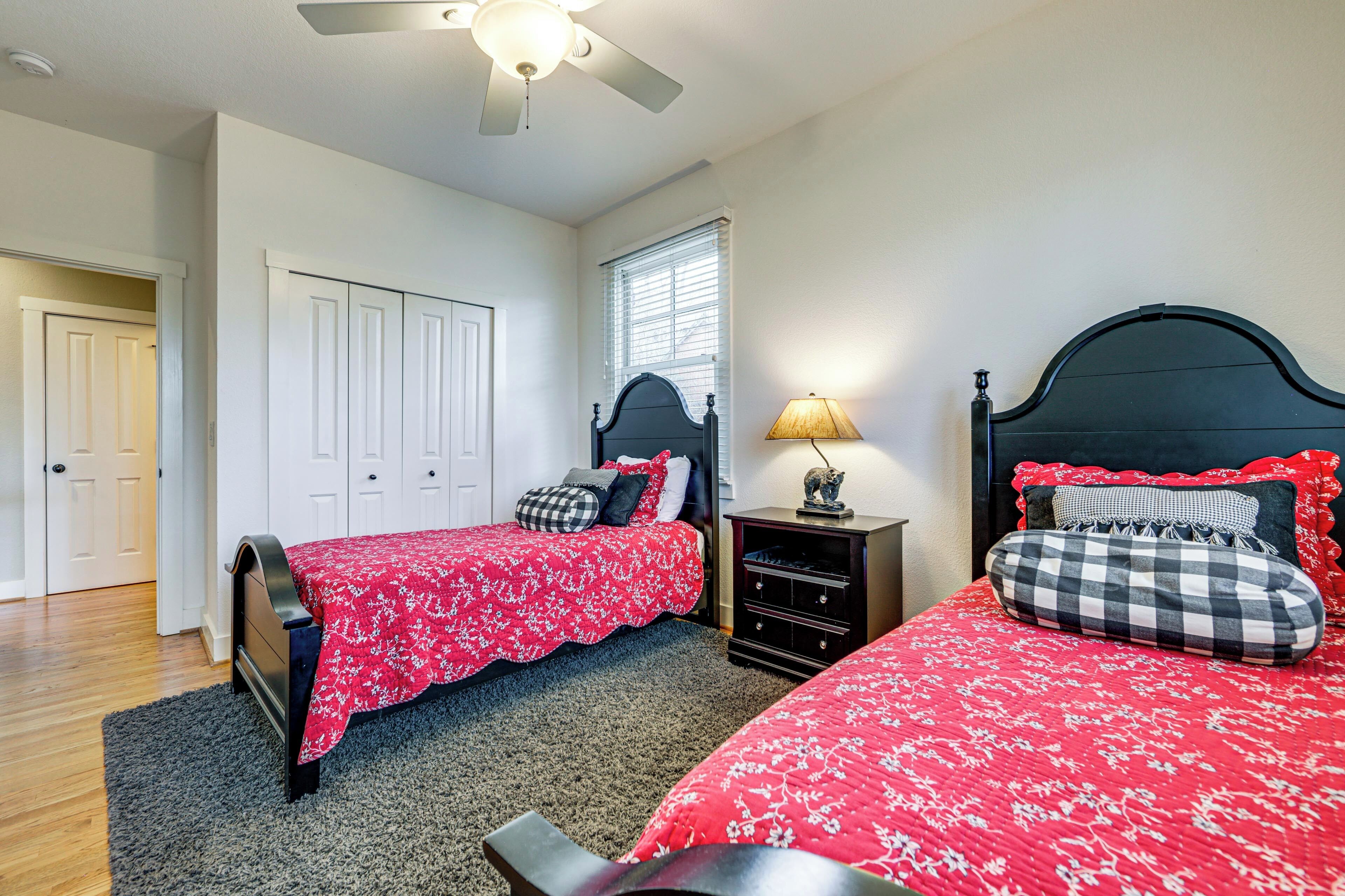 A bedroom with two beds, a ceiling fan, a nightstand with a lamp, and a window with blinds.