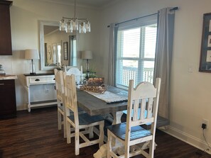 A dining area with a wooden table, white chairs, and a chandelier. - The Salty Pelican Lodge - New construction in Hackberry (Hackberry)