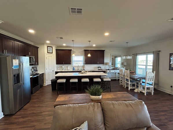 A spacious kitchen with dark wood cabinets, a central island with bar stools, and a dining area with white chairs. - The Salty Pelican Lodge - New construction in Hackberry (Hackberry)