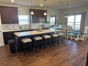 A modern kitchen with dark wood cabinets, a large island with bar stools, and pendant lighting. - The Salty Pelican Lodge - New construction in Hackberry (Hackberry)