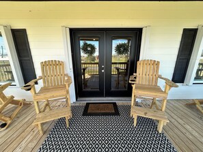 A wooden deck with two Adirondack chairs, a black and white patterned rug, and a black door with a wreath. - The Salty Pelican Lodge - New construction in Hackberry (Hackberry)
