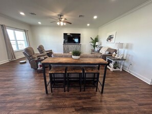 A spacious living room with a wooden dining table, multiple seating options, a ceiling fan, and a flat-screen TV. - The Salty Pelican Lodge - New construction in Hackberry (Hackberry)