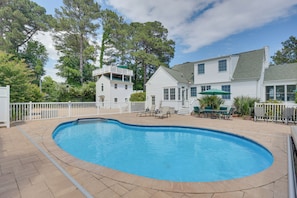 A swimming pool with a white fence, a covered patio area, and a two-story house with a balcony.