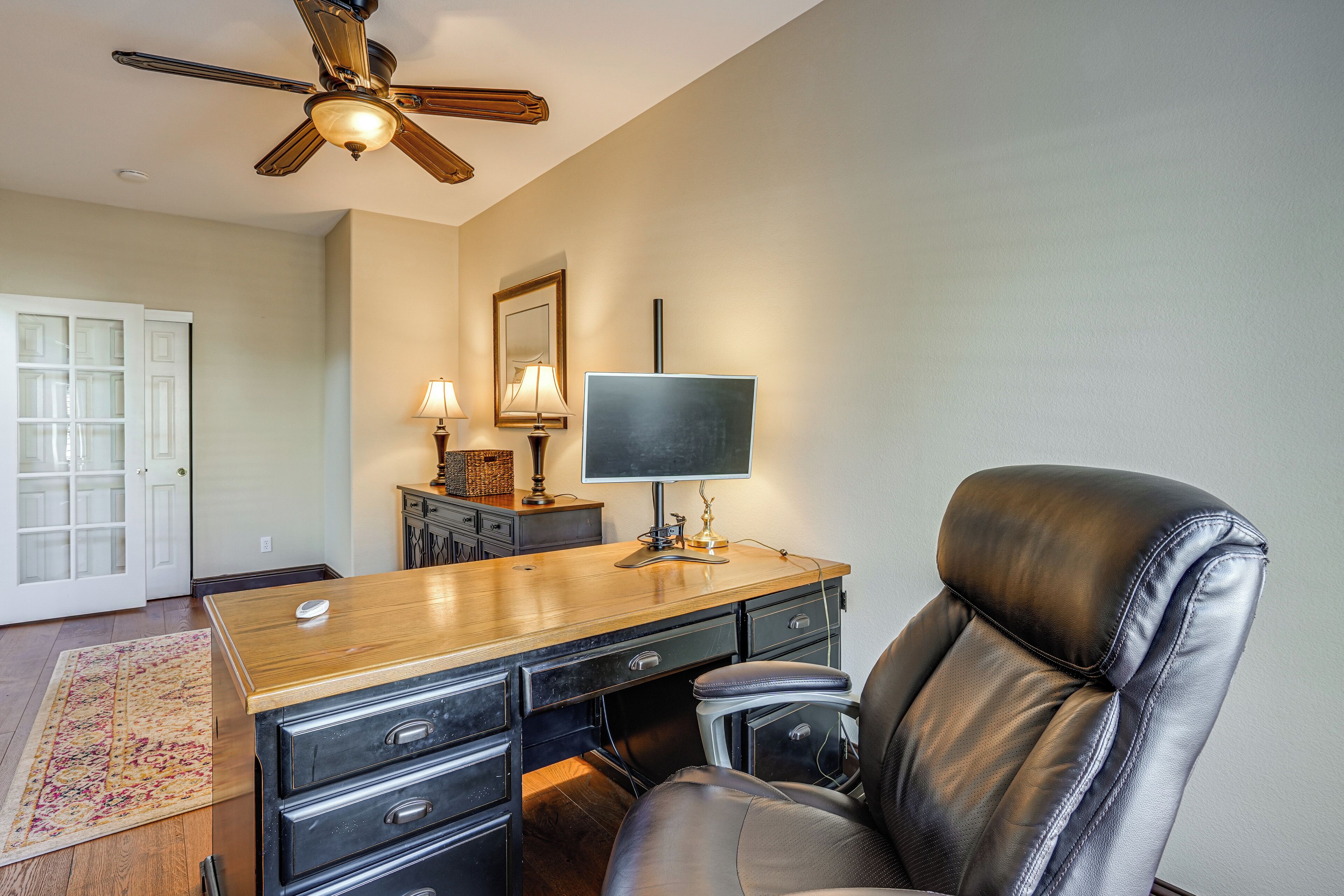 A home office with a desk, leather chair, ceiling fan, and a large window.