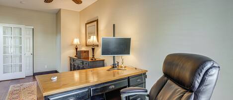 A home office with a desk, leather chair, ceiling fan, and a large window.