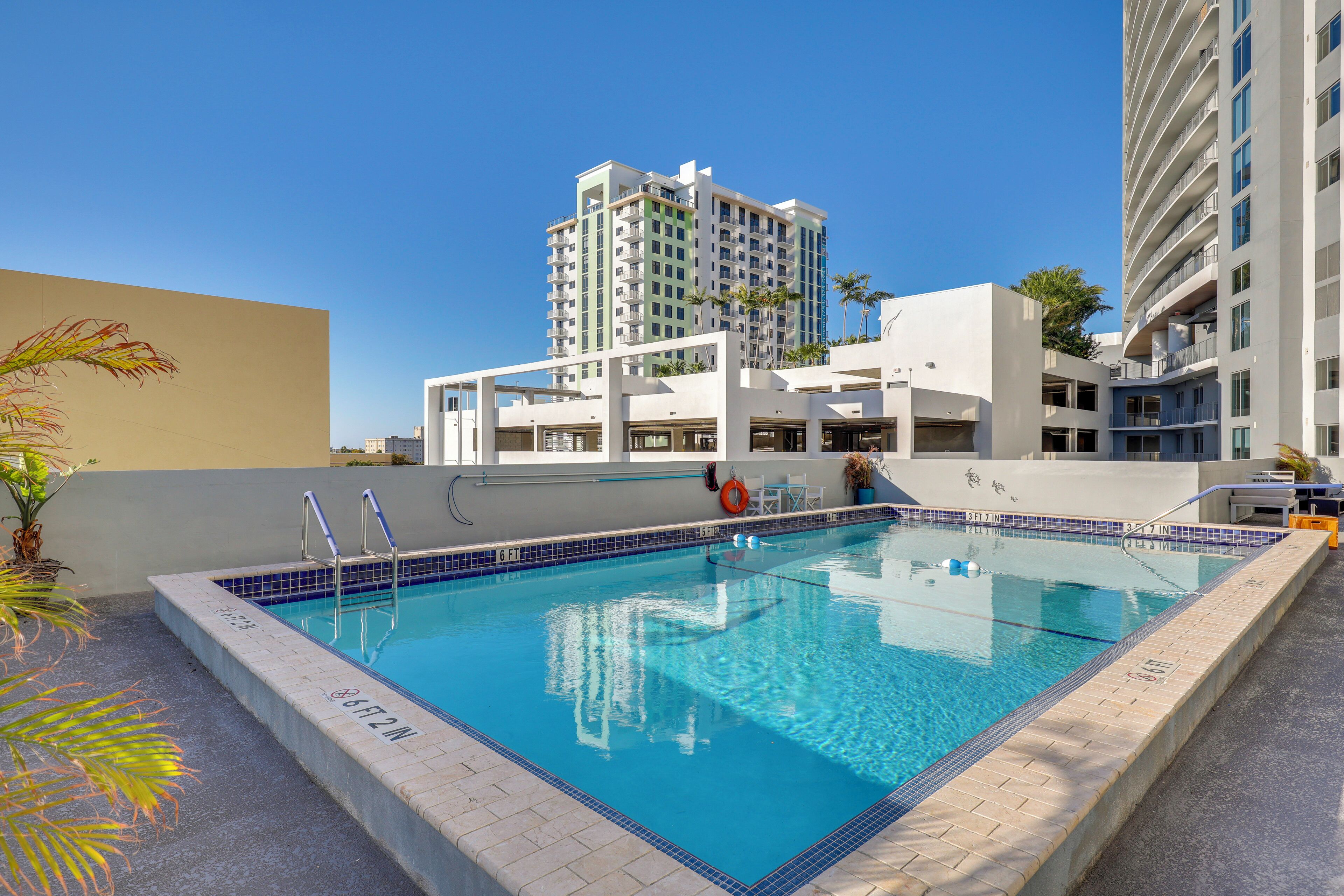 A swimming pool with clear blue water, surrounded by a tiled deck and a white building with balconies.