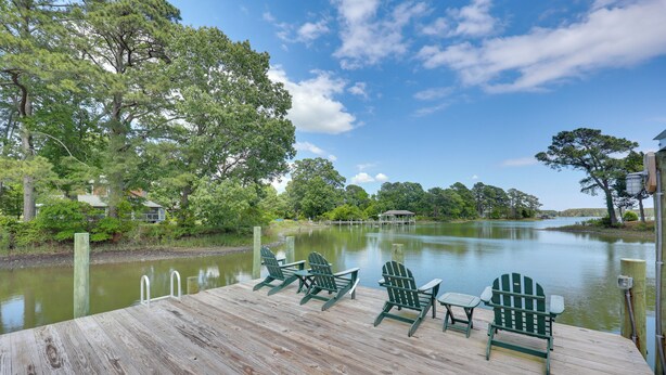 A wooden dock with green Adirondack chairs and a view of a lake.