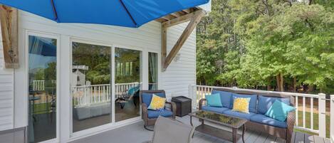 A covered deck with a blue umbrella, wicker furniture, and a glass door leading to a deck area.
