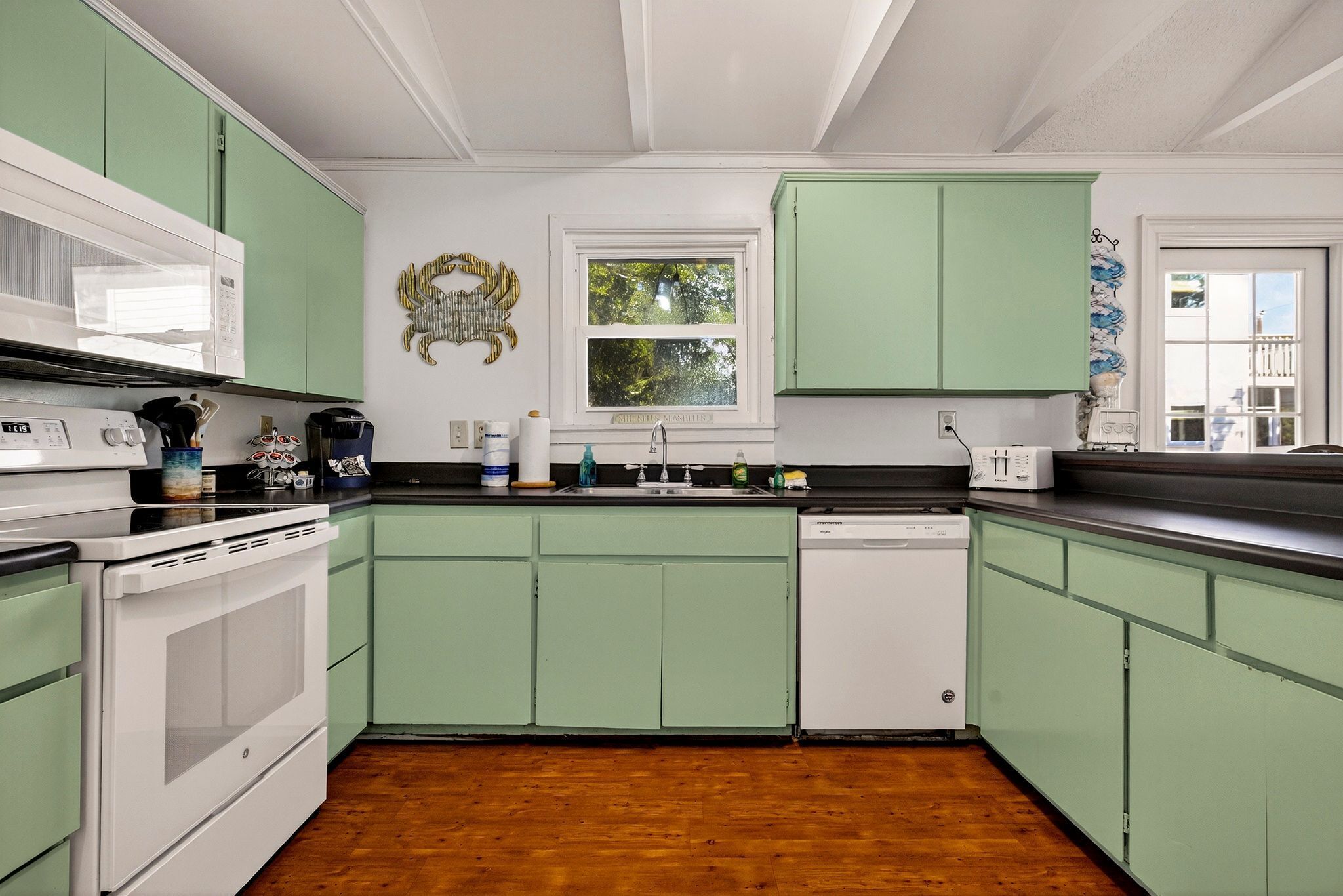 A kitchen with green cabinets, a white stove, a microwave, and a dishwasher.