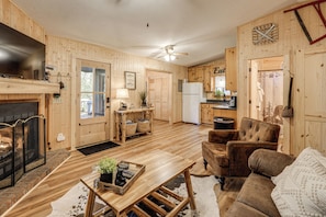 A cozy cabin-style interior with a fireplace, wooden furniture, and a kitchen area. - 5 Mi to Helen: Woodsy Oasis w/ Hot Tub & Fire Pit! (Sautee Nacoochee)