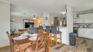 Uma cozinha moderna com armários brancos, micro-ondas e fogão. Há uma área de refeições com uma mesa e cadeiras de madeira.