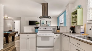 A modern kitchen with white cabinetry, a built-in stove, and a green shelf with glassware. - Perfect for Small Families, Steps to Beach and Dining by Tybee Cottages (Savannah)