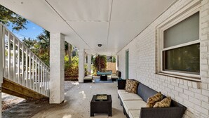 A covered patio area with a concrete floor, a black coffee table, a beige sofa, and a white railing. - Perfect for Small Families, Steps to Beach and Dining by Tybee Cottages (Savannah)