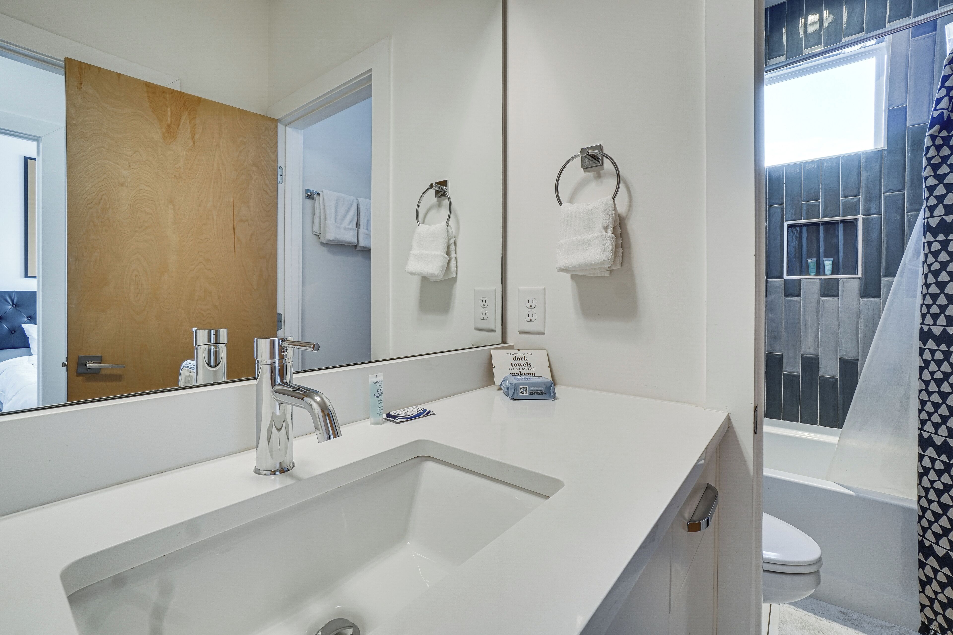 A modern bathroom with a large mirror, white sink, and a shower area.