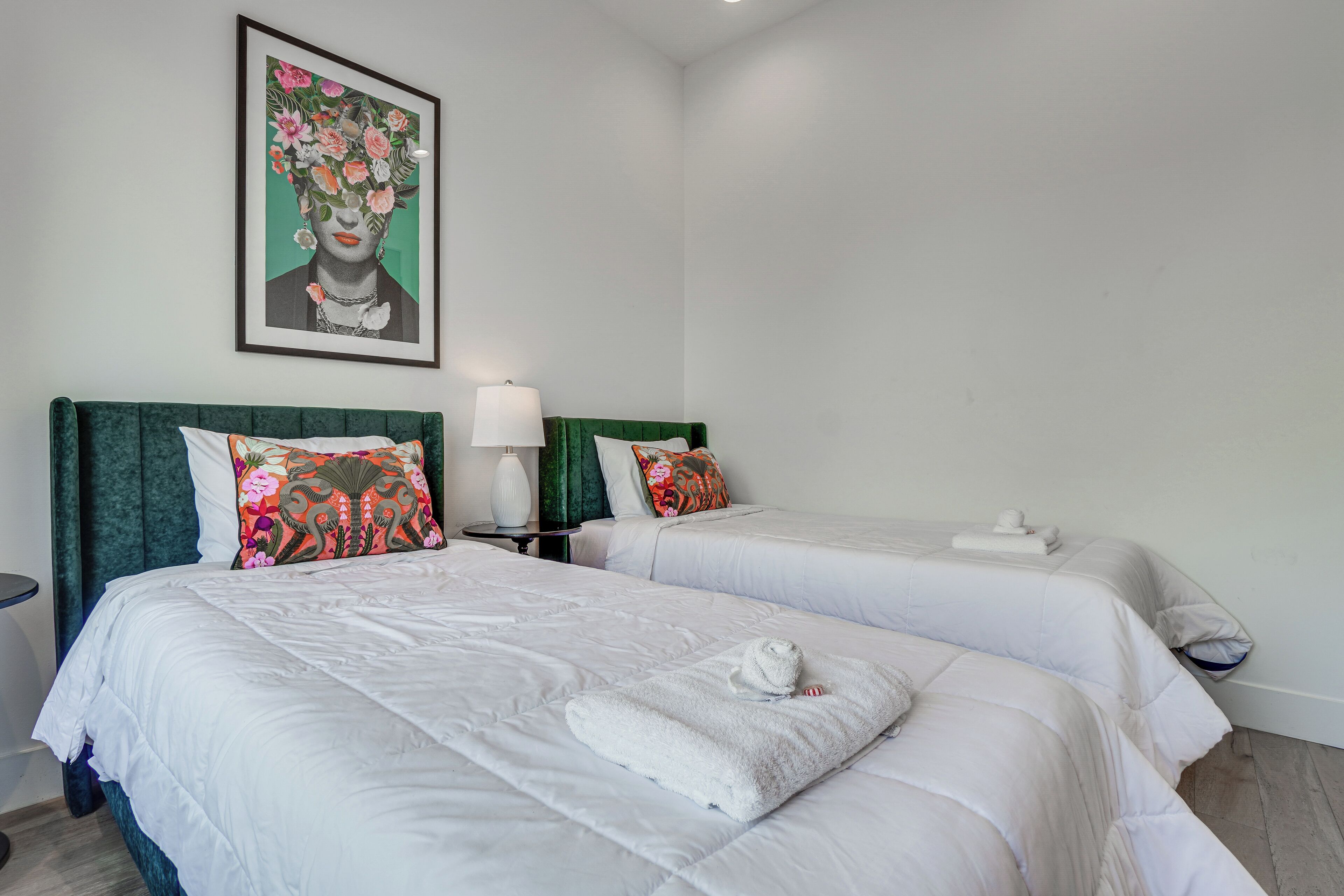 A hotel room with two beds, each with white bedding and decorative pillows. A framed artwork is on the wall above the beds.