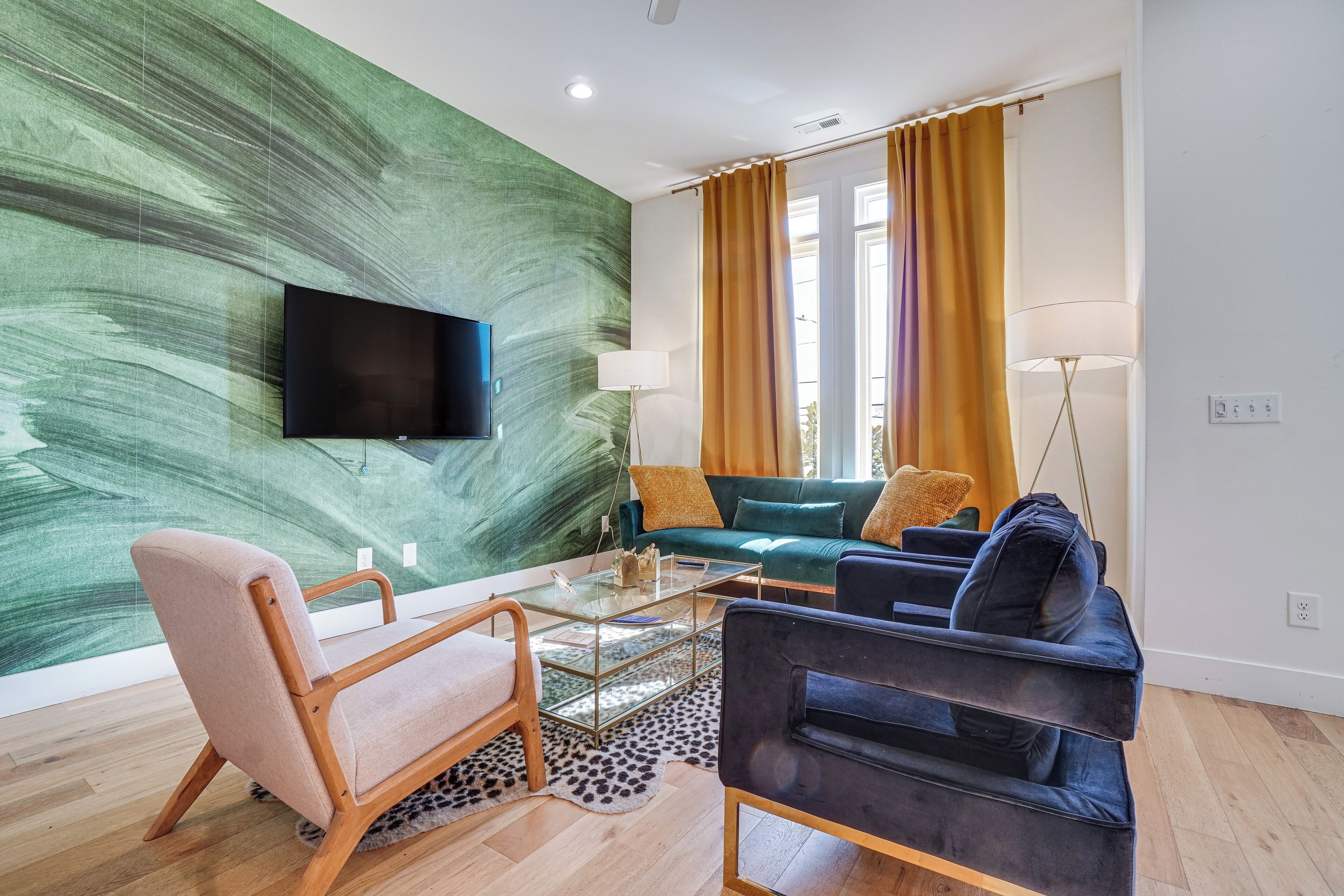 Ein modernes Wohnzimmer mit einem an einer grünen, strukturierten Wand montierten Flachbildfernseher, einer Couch, einem Couchtisch und einer Stehlampe.