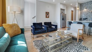 A modern living room with a teal sofa, two blue armchairs, a glass coffee table, and a leopard print rug. - 1 Mi to Nashville General: Upscale Townhome (Nashville)