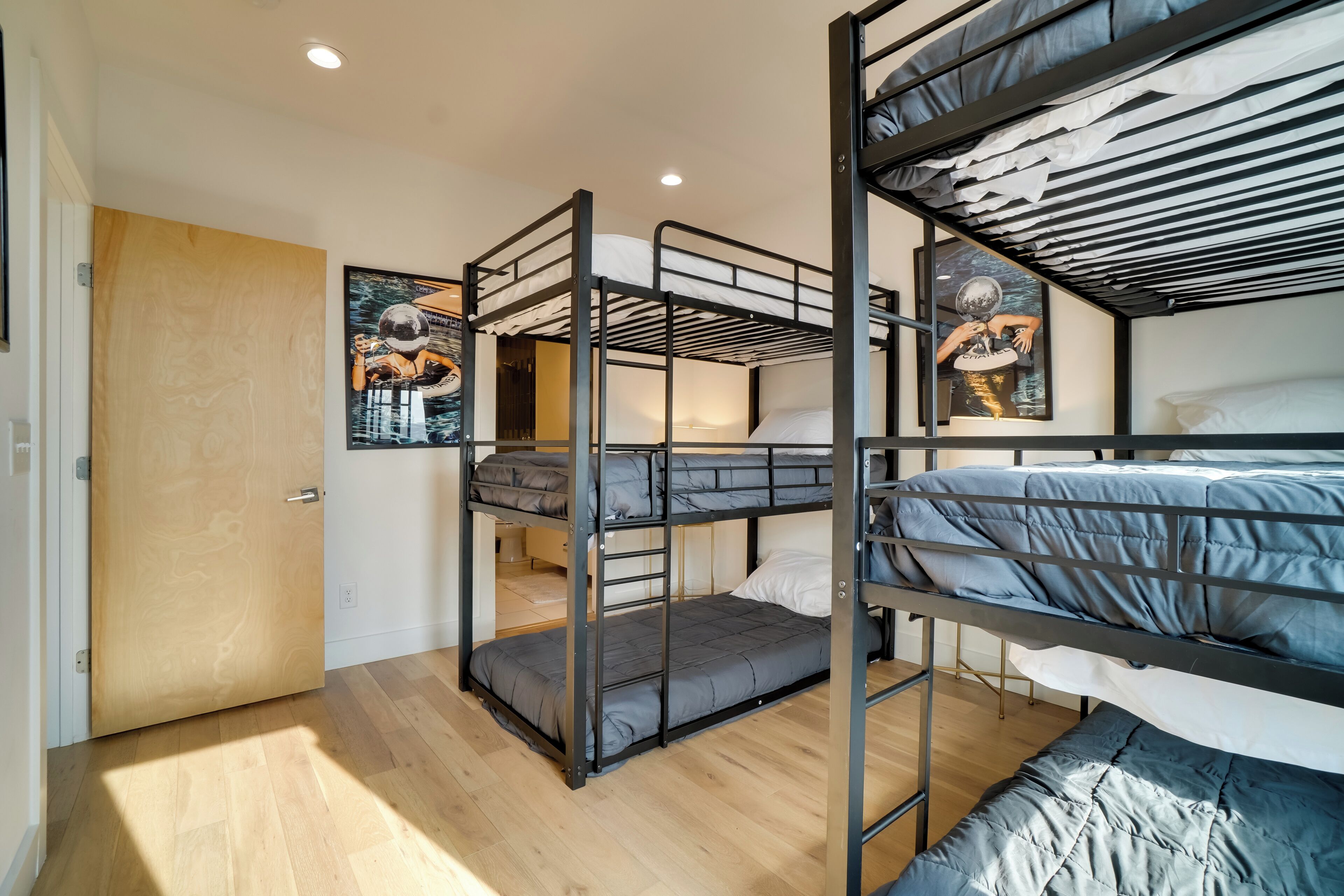 A bunk bed room with a wooden door, a framed artwork on the wall, and a light-colored floor.