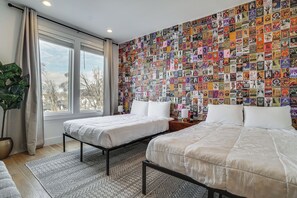 Ein Zimmer mit zwei Betten, einem großen Fenster und einer Wand voller bunter Plakate.