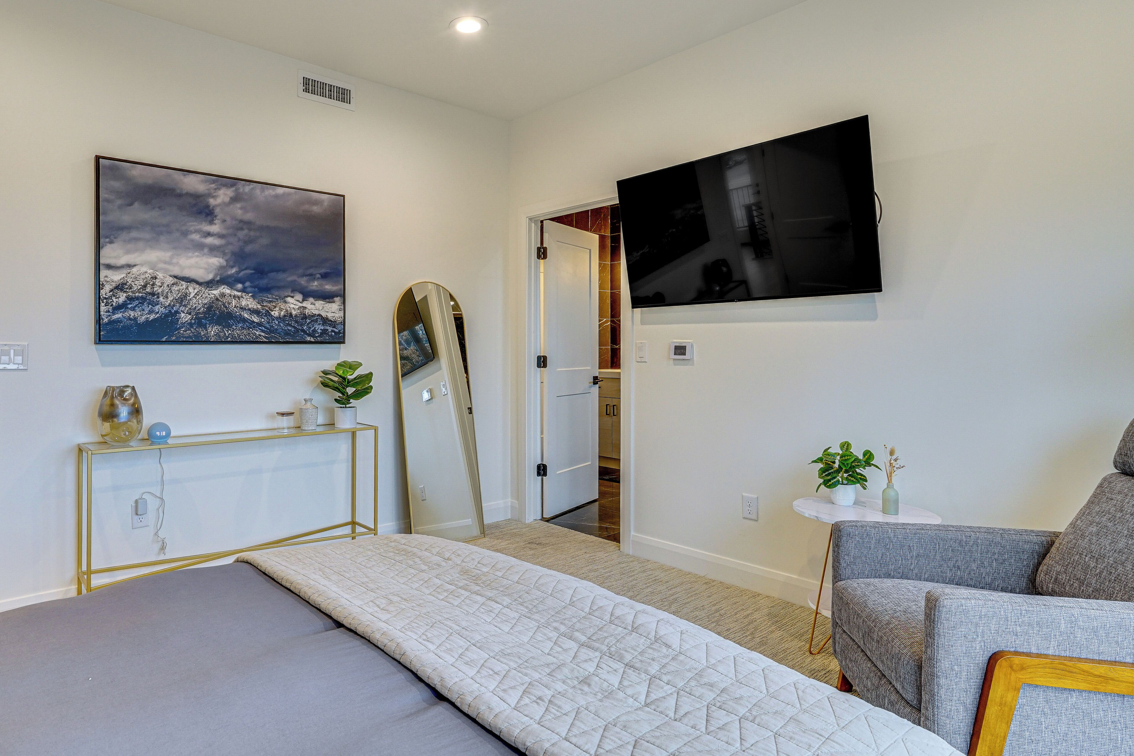 Une chambre à coucher moderne avec un lit, une télévision, un tableau et une console sur laquelle est posée une plante.