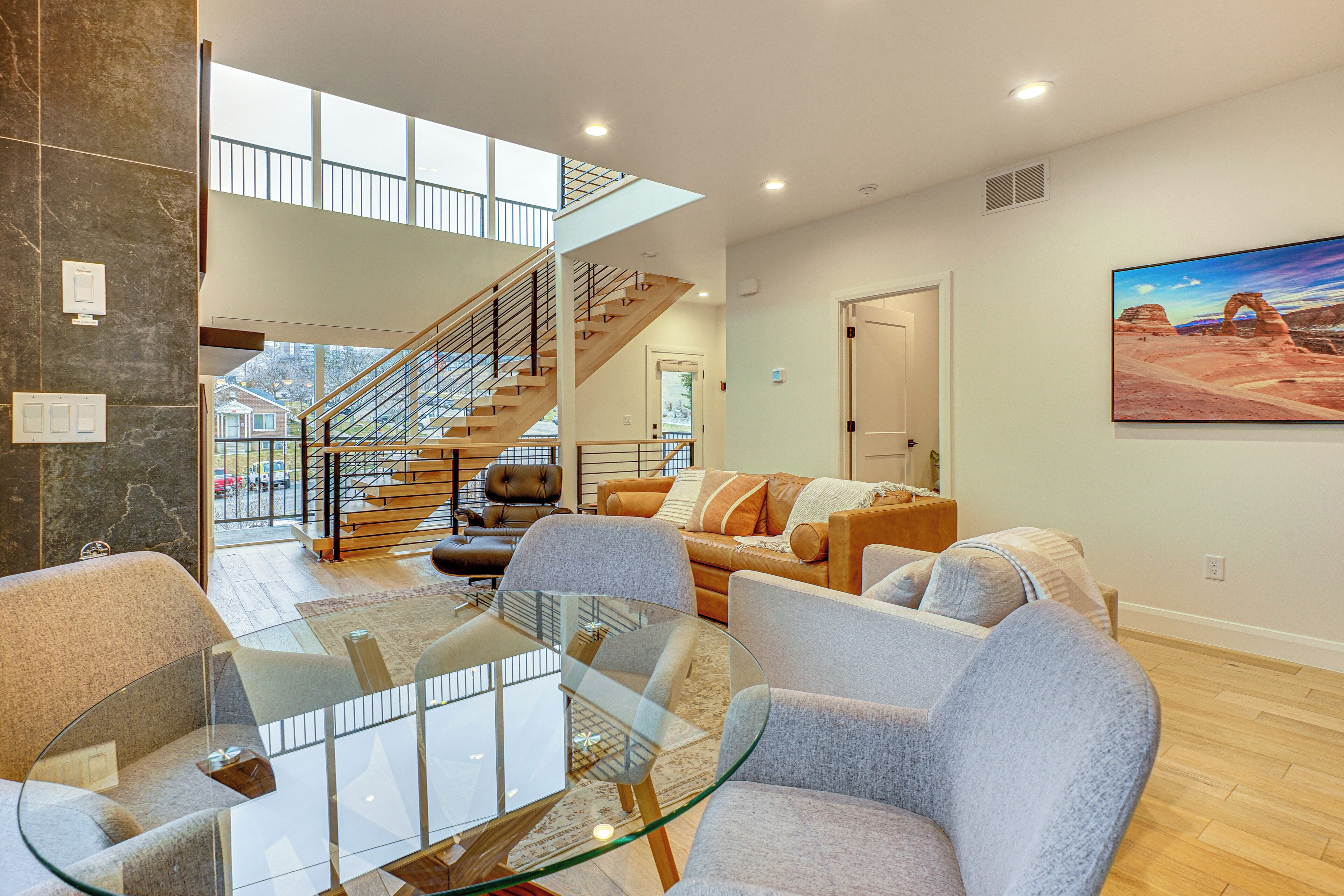 A spacious living room with a glass coffee table, grey sofas, and a staircase leading to an upper level.