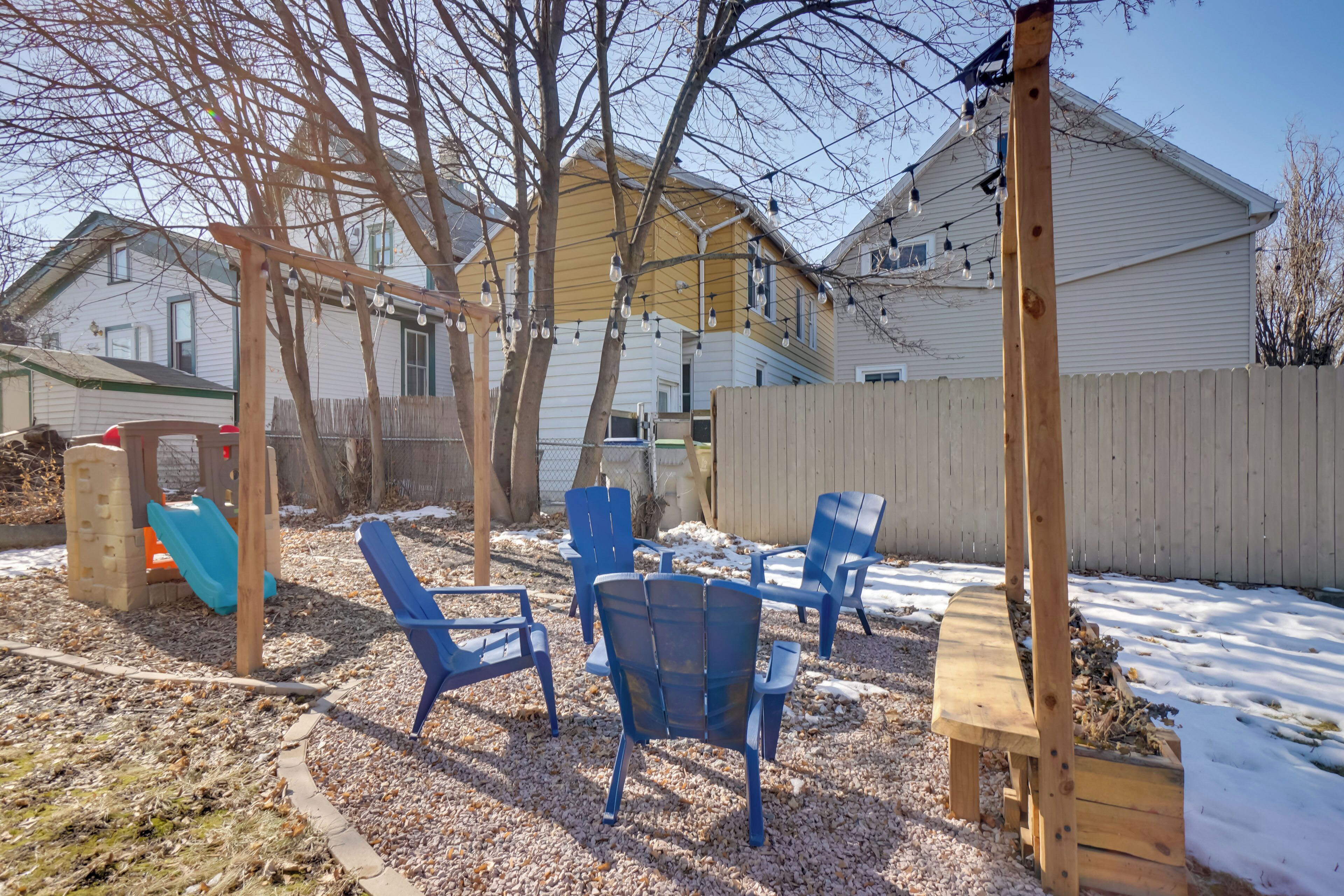 A backyard with a wooden swing set, blue chairs, and a wooden bench.