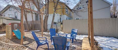 A backyard with a wooden swing set, blue chairs, and a wooden bench.