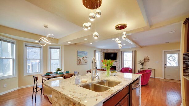 A spacious kitchen with a marble countertop, double sink, and a large island. There are pendant lights hanging from the ceiling and a flat-screen TV mounted above the island. - Walk to Kinnickinnic Ave! Newly Updated Abode (Milwaukee)