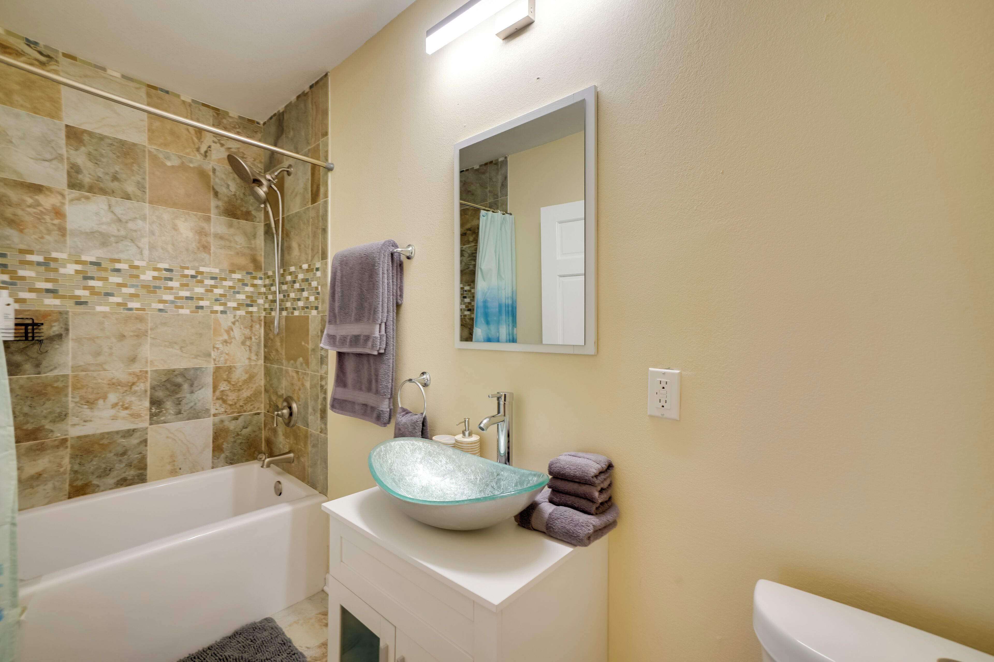 Une salle de bain avec une baignoire, un lavabo en verre, une douche et des toilettes.