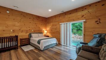 A room with a bed, a chair, a small table, and a window with a view of greenery.
