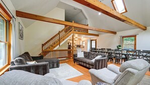 Un vaste espace de vie doté d’un plafond haut, de poutres en bois, d’un escalier et d’un coin repas avec plusieurs chaises et une table.