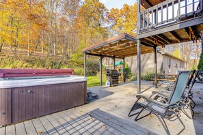 Eine Holzterrasse mit Whirlpool, Sitzgelegenheiten im Freien und einem überdachten Bereich mit Grill.