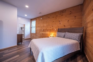Une chambre avec un mur en bois, un lit, une table de chevet et une fenêtre.