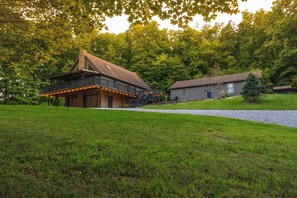 Eine rustikale Holzhütte mit Balkon und Lichterkette, umgeben von üppigem Grün.