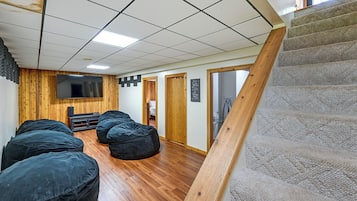 A room with a wooden floor, a flat-screen TV mounted on the wall, and a staircase with a wooden handrail.