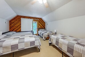 Une chambre avec deux lits, des poutres apparentes en bois au plafond, une fenêtre avec des rideaux et un ventilateur de plafond.