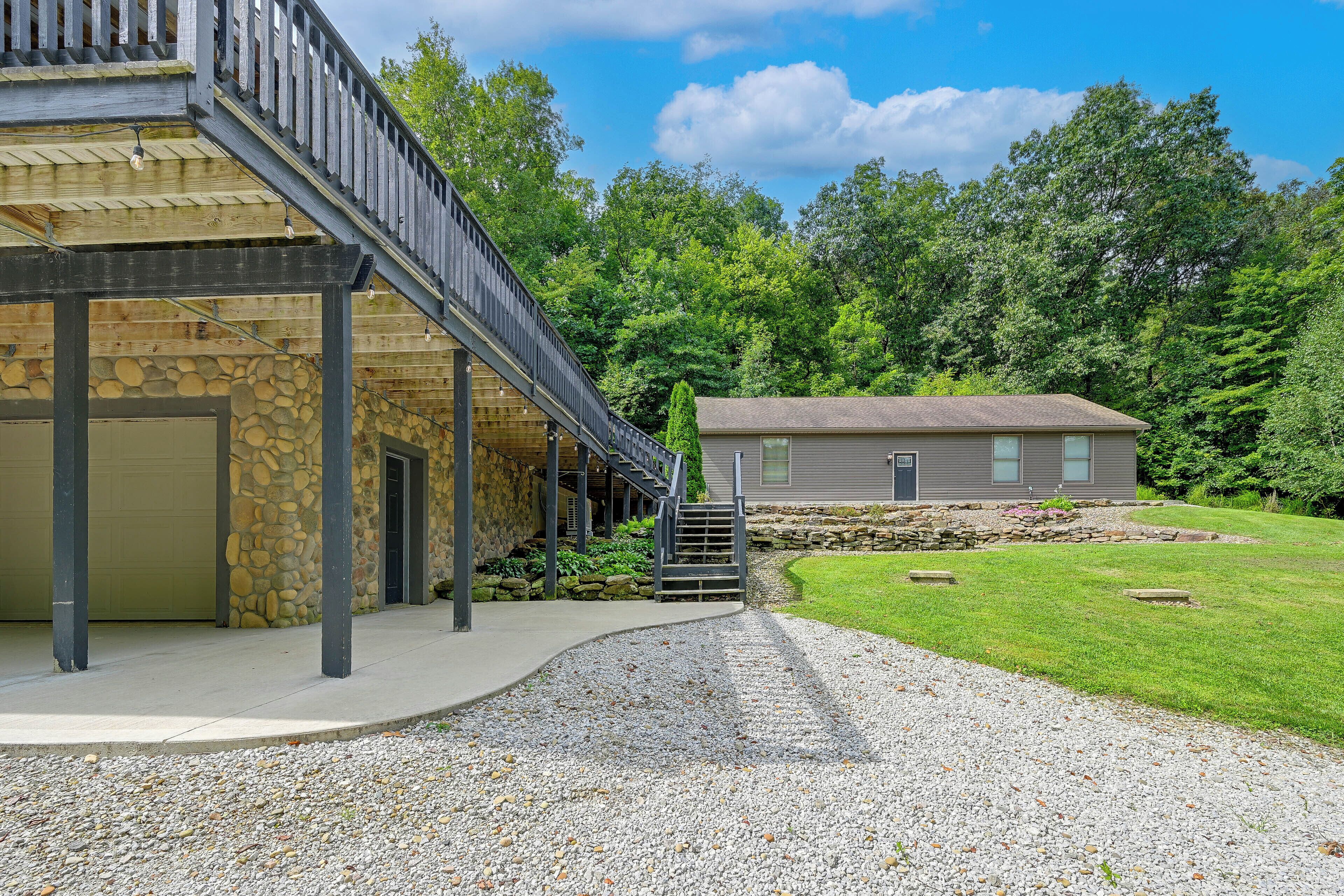 A building with a stone facade, a covered outdoor area, and a gravel driveway leading to a house with a sloped roof.
