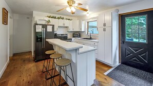 Une cuisine moderne avec des meubles blancs, un îlot central doté de tabourets, un réfrigérateur, un four et un four à micro-ondes.