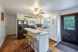 Eine moderne Küche mit weißen Schränken, einer zentralen Kochinsel mit Barhocker, einem Kühlschrank, einem Backofen und einer Mikrowelle.
