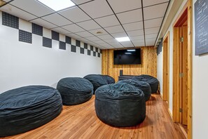 Une pièce avec un plancher en bois, des fauteuils en forme de sac de haricots noirs, un téléviseur à écran plat fixé au mur et une porte en bois.