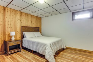 Ein Schlafzimmer mit Holzkopfteil, einem Bett mit gesteppter Decke, einem Nachttisch mit Lampe und einem Fenster mit Tageslicht.