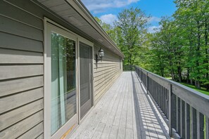 A wooden deck with a railing, a glass door, and a wall-mounted light fixture. - Shady Point Retreat w/ Hot Tub & Pickleball! (Killbuck)