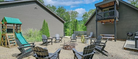 A backyard with a fire pit, Adirondack chairs, a slide, and a barbecue area.