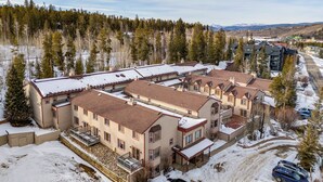 A multi-story residential building with a snow-covered roof and a driveway with parked cars. - Pool & Hot Tub! Hub for All-season Winter Park Fun (Winter Park)